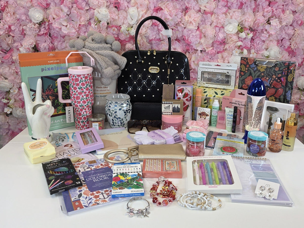 The giveaway haul: a Brangio Italy handbag, rose tumbler, sherpa blanket, glitter lamp, jewelry, makeup, spa items, stationery and candy spread out on a table in front of a pink flower wall